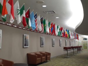 International Hall at COD. Wide shot of flags hanging from wall, student story portraits, and chairs.