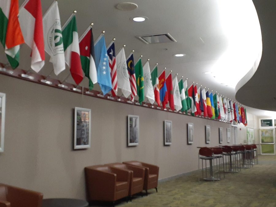 International Hall at COD. Wide shot of flags hanging from wall, student story portraits, and chairs.