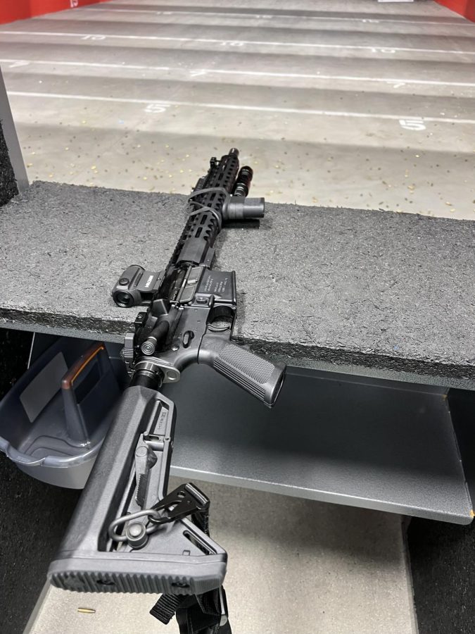 A photo of an AR-15 laying on the window of a booth at a gun range.