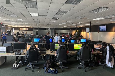 Students sitting at rows of tables lined with PC's playing the game Valorant