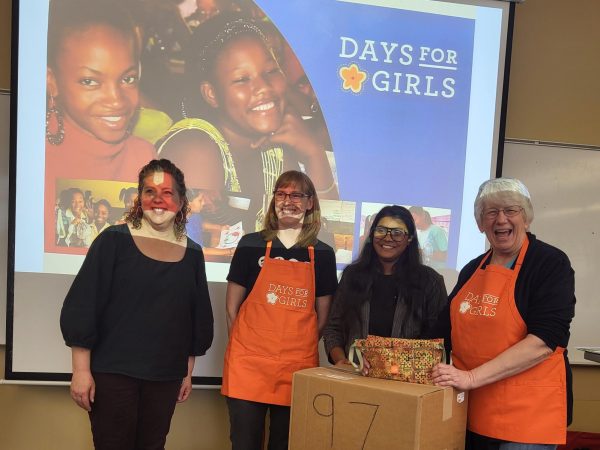 Student Masuda Moutushi and Days for Girls leaders stand by boxes of ninety-seven donation packages.