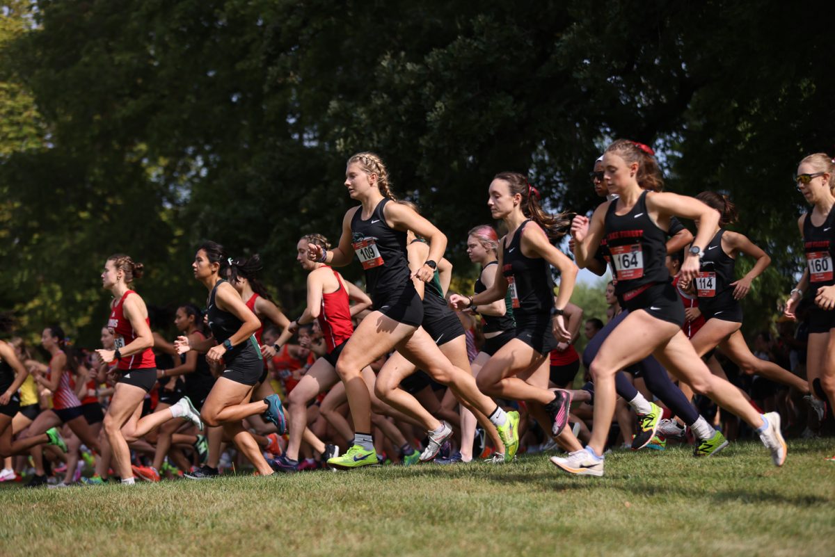 The women’s cross country team runs from the starting line. 

