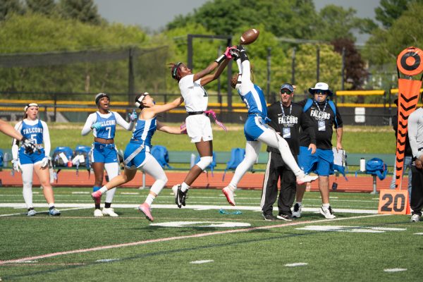 Number 18, Destynee McCoy jumping to catch a football while a defensive player also jumps to intercept.
